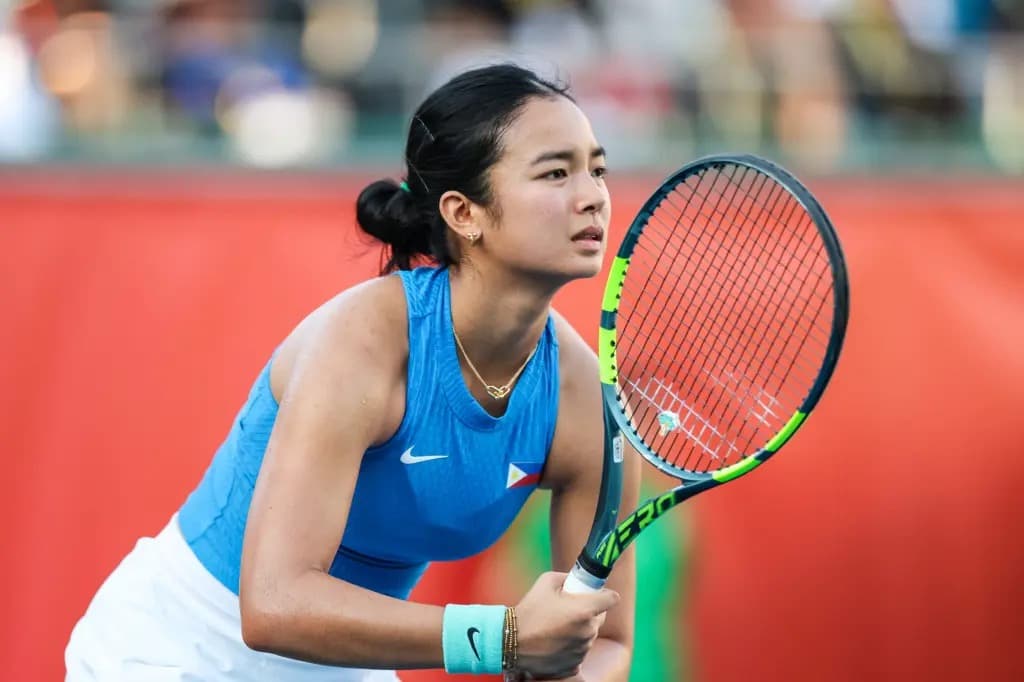 Alex Eala in a Philippines jersey holding a tennis racket, focused on the court.