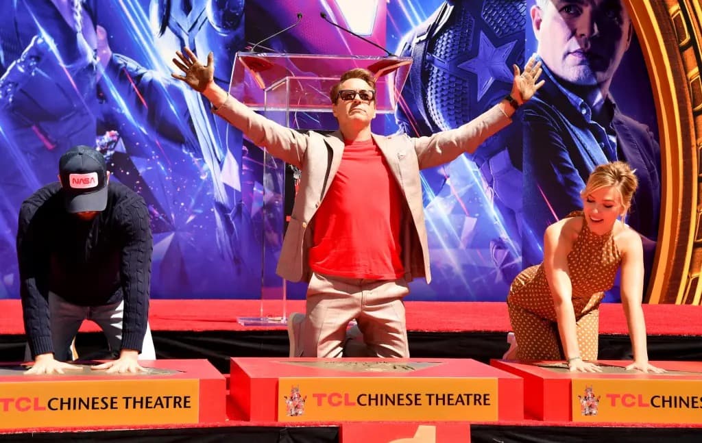 Robert Downey Jr. raising his arms at a handprint ceremony at the TCL Chinese Theatre, flanked by two other people.