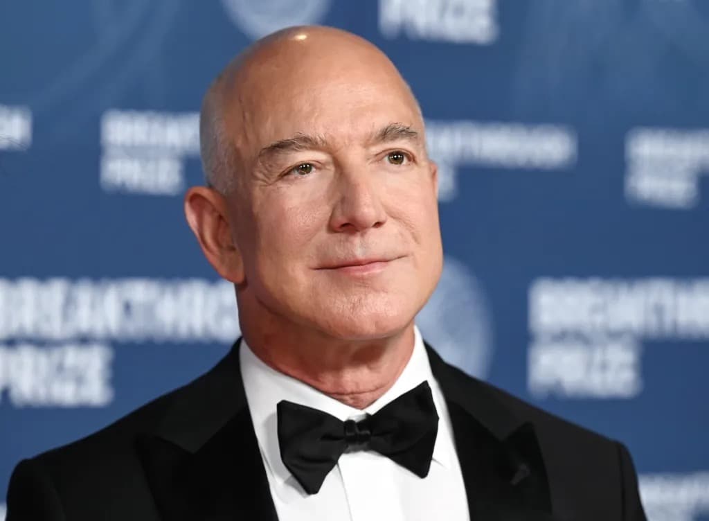 Jeff Bezos in a tuxedo at an evening event, smiling in front of a blue backdrop.