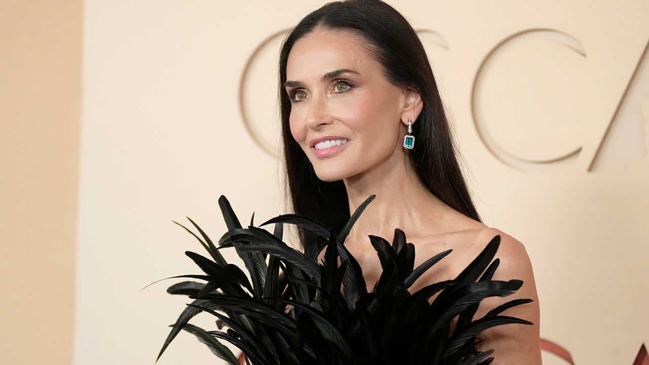 Demi Moore poses on the red carpet at the Oscars in a black feathered gown.