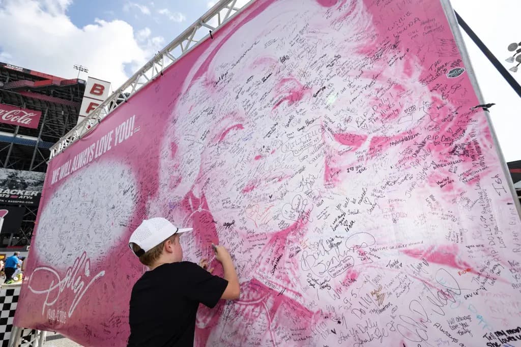 A young fan signs a large pink memorial banner for Dolly Parton reading 'We Will Always Love You,' 1946-2026.