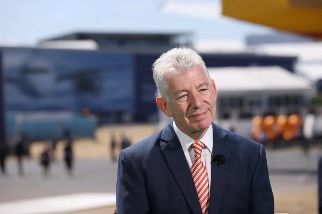 Paul Griffiths in a navy suit and striped tie, standing on an airport tarmac.