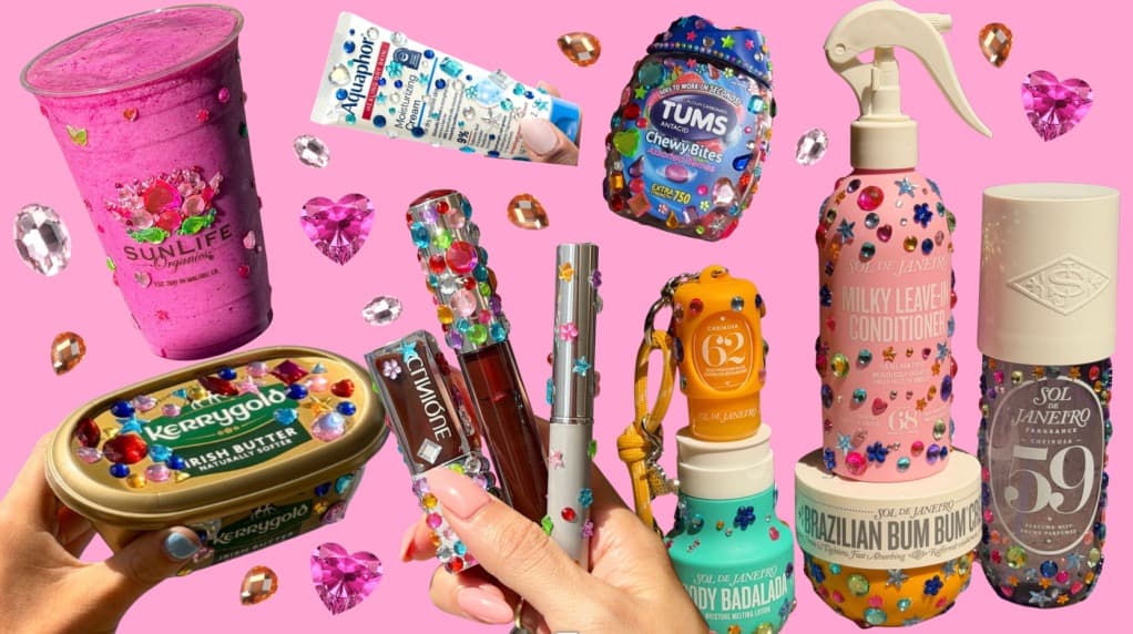 A flat lay of rhinestone-covered beauty and food products, including a smoothie cup, lip gloss, hair products, and a tub of butter, on a pink background.