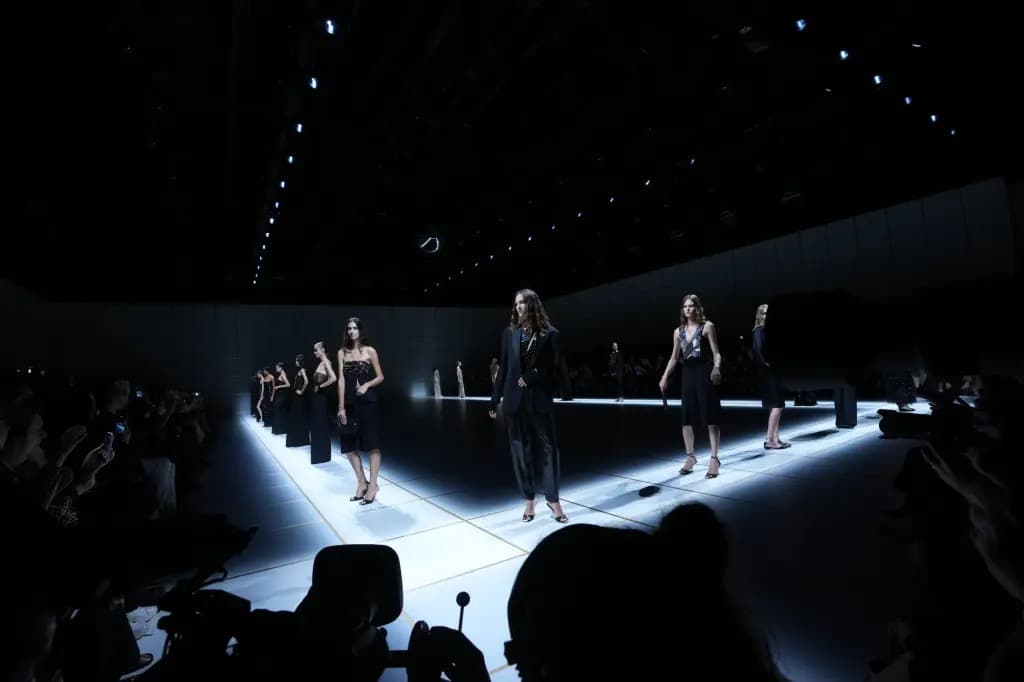 Models walking a dark, illuminated runway at an Armani fashion show.