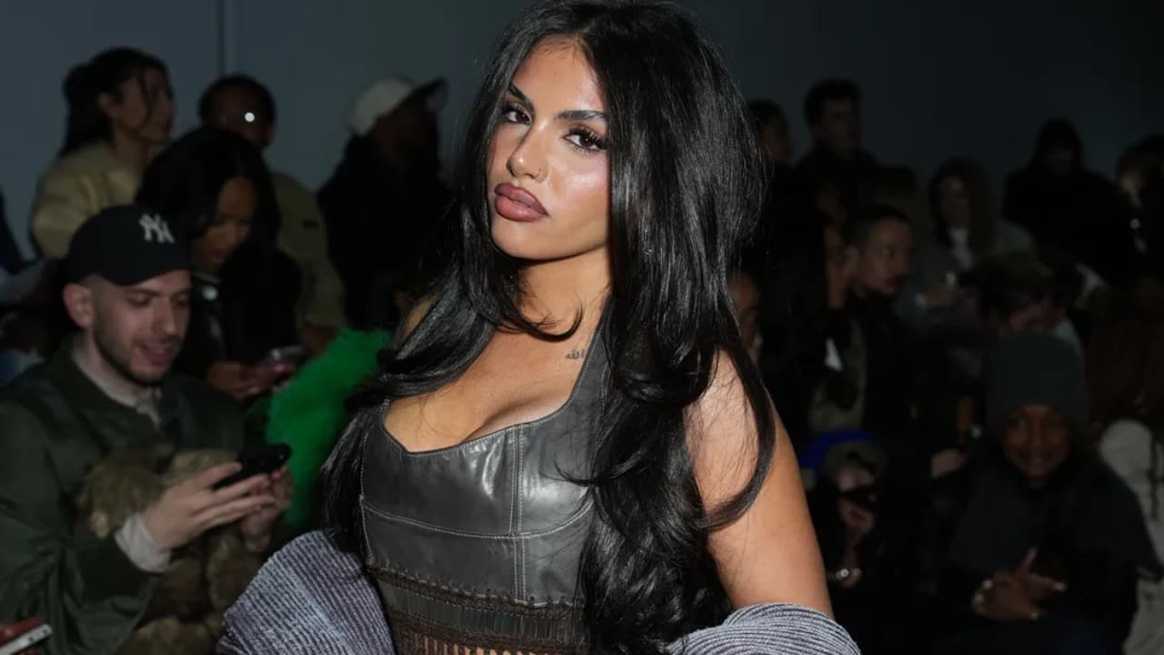Huda Mustafa poses at an event wearing a grey leather top with long dark hair.