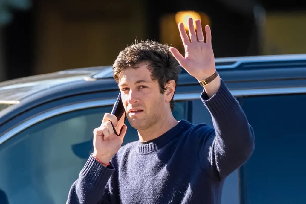 Josh Kushner waving while holding a phone to his ear, standing next to a car.