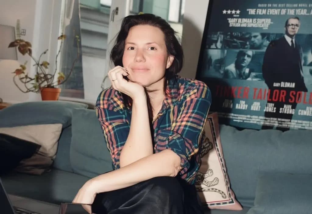 Kate Dohaney smiling with her chin resting on her hand, seated on a couch.