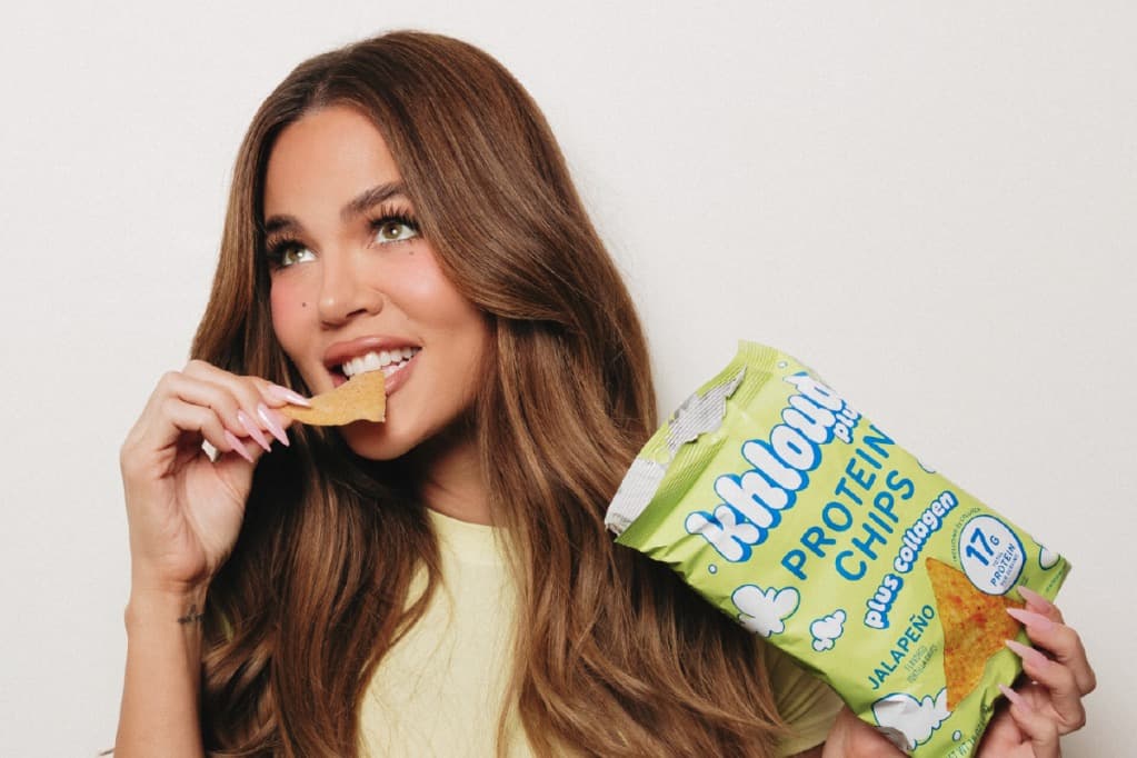 A woman eating a protein tortilla chip while holding a bag of Khloud Plus Collagen Protein Chips.