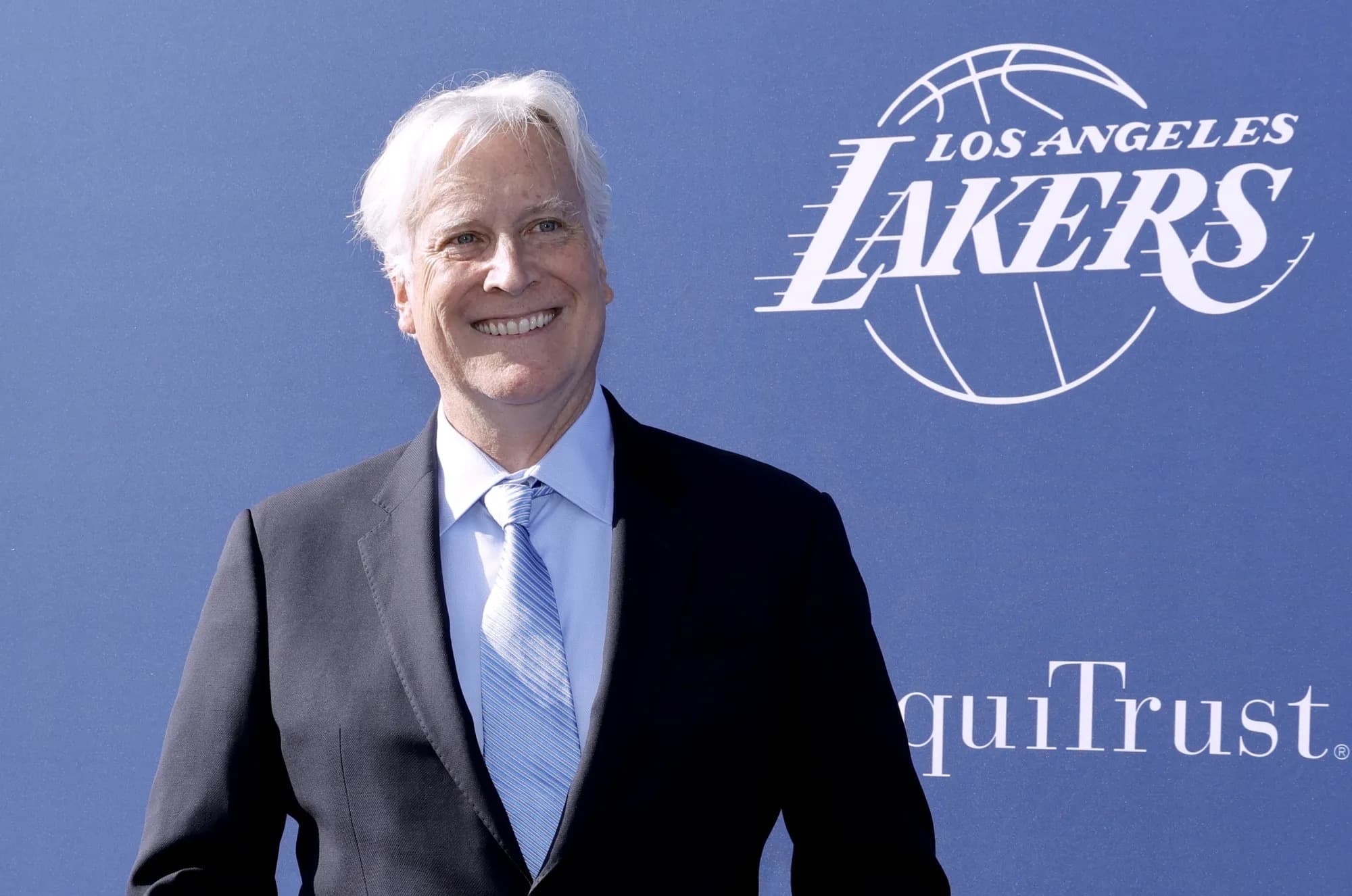 Mark Walter smiling in a suit and tie in front of a Los Angeles Lakers backdrop.