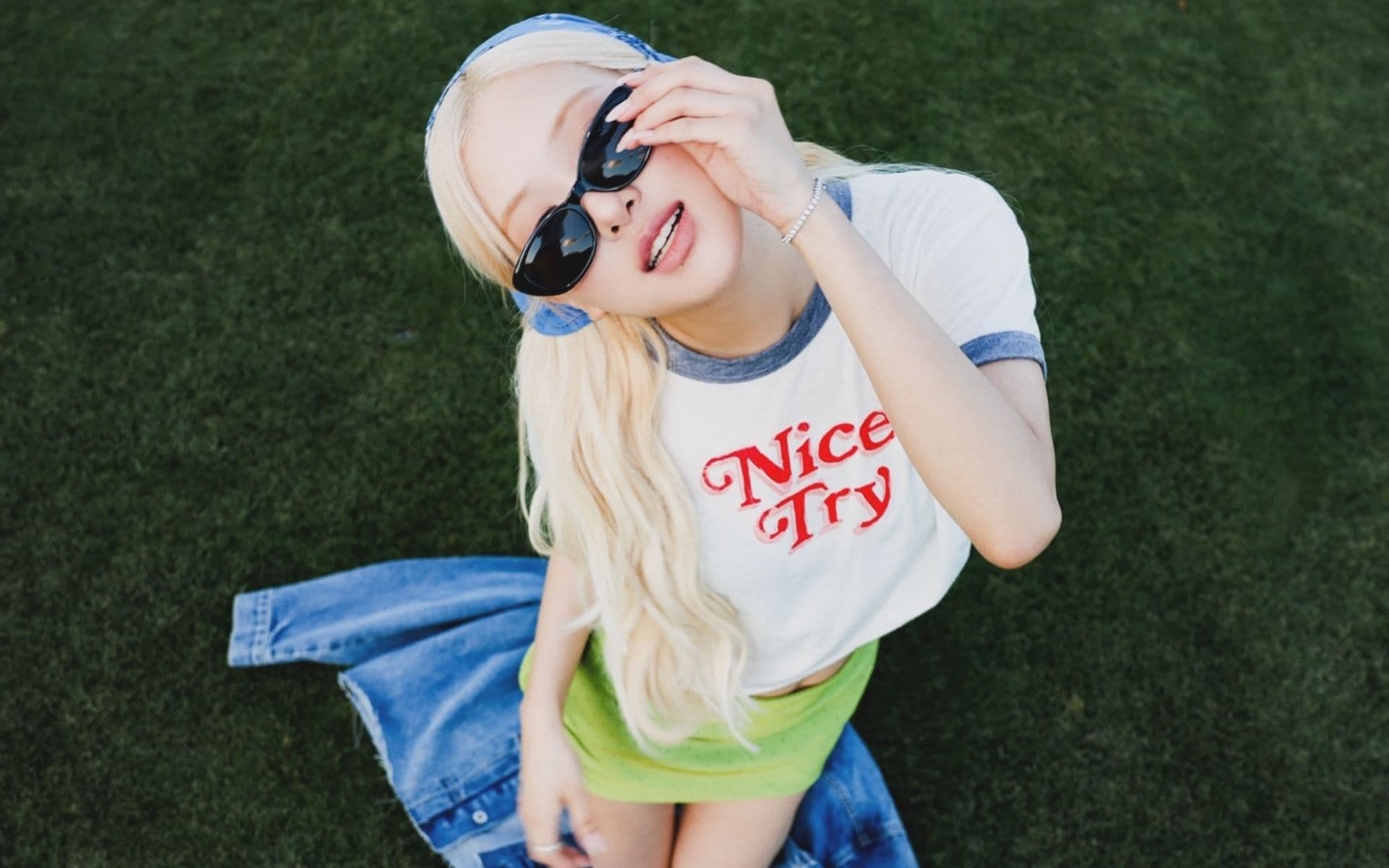 A woman in sunglasses wears a white and blue ringer tee reading "Nice Try" over a green skirt.