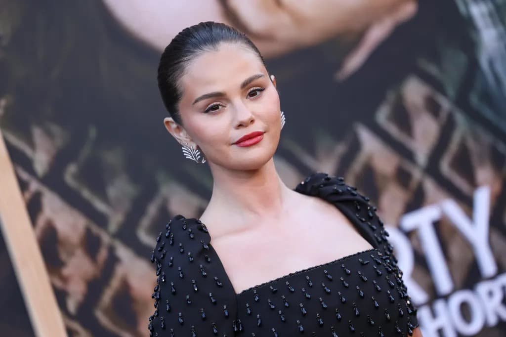 Selena Gomez smiling on a red carpet in a black beaded dress.