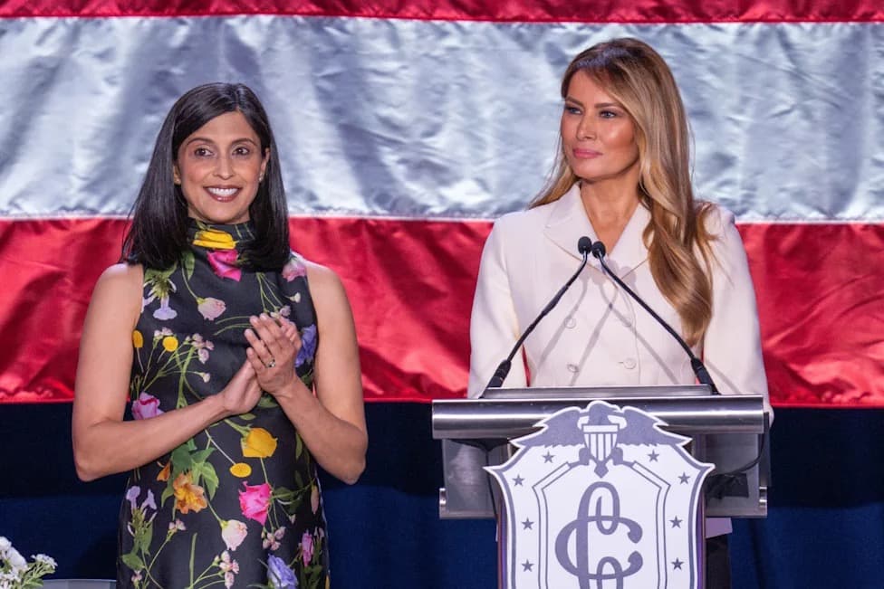 Usha Vance smiling in a floral dress, standing beside Melania Trump at a podium.